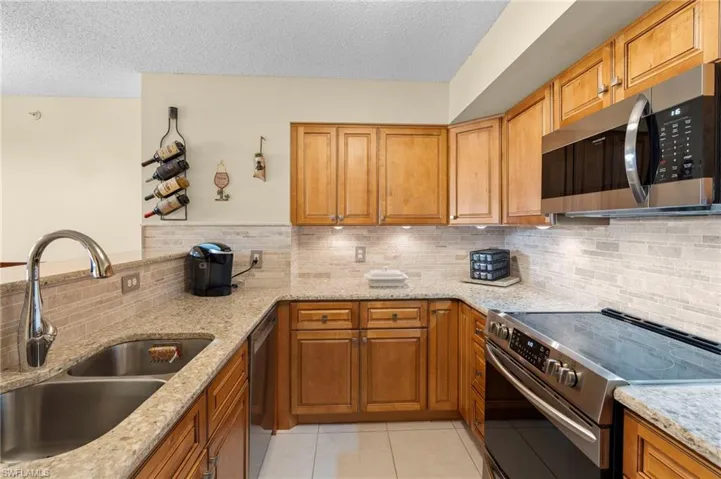 Kitchen featuring sink, decorative backsplash, appliances with stainless steel finishes, light tile patterned floors, and light stone countertops