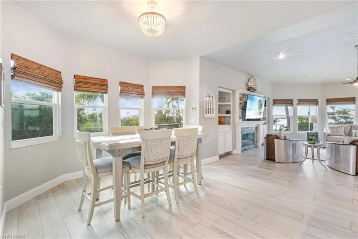 Dining area with light wood finished floors, a textured ceiling, a tiled fireplace, a ceiling fan, and a chandelier