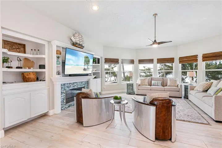 Living area featuring a textured ceiling, a ceiling fan, a tile fireplace, light wood finished floors, and built in shelves
