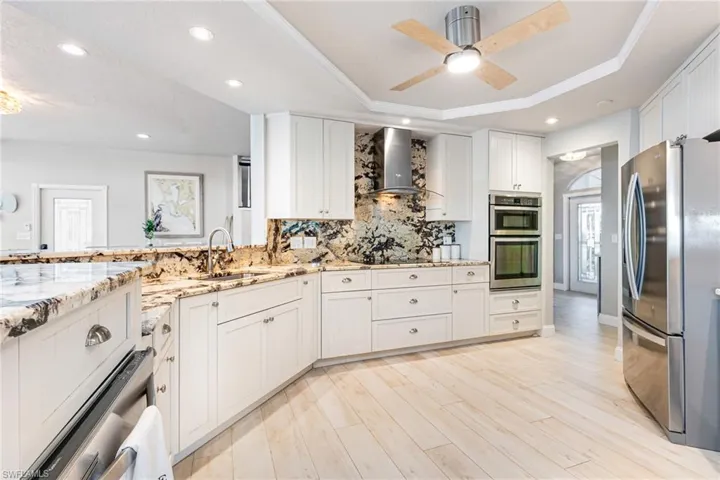 Kitchen featuring stainless steel appliances, white cabinetry, wall chimney range hood, light stone countertops, and light wood-type flooring