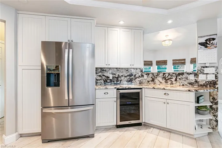 Kitchen featuring stainless steel fridge, open shelves, beverage cooler, white cabinets, and light stone counters