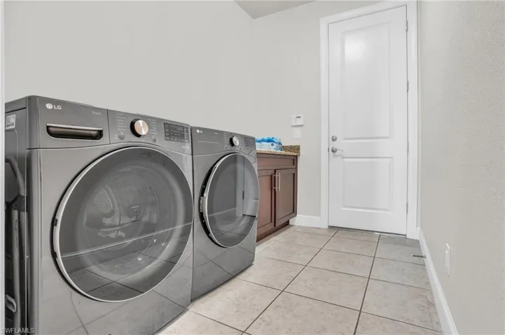 Laundry room with separate washer and dryer, light tile floors, and cabinets