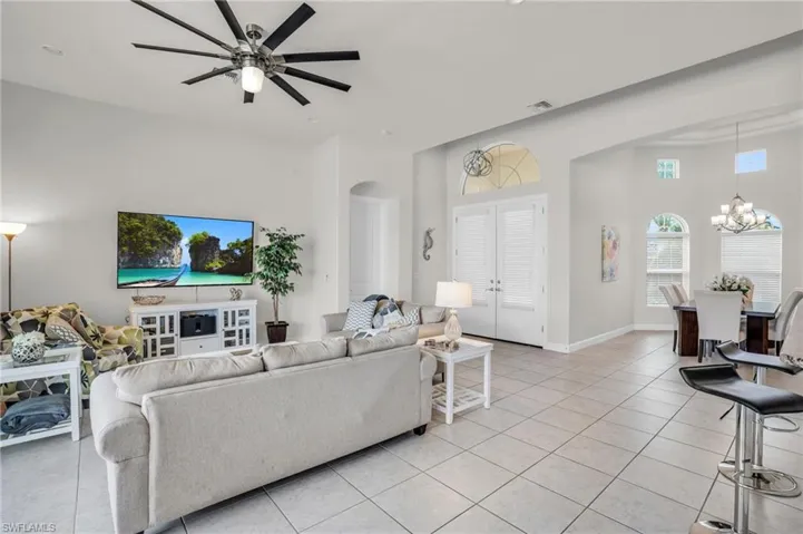 Living room with ceiling fan with notable chandelier and light tile floors