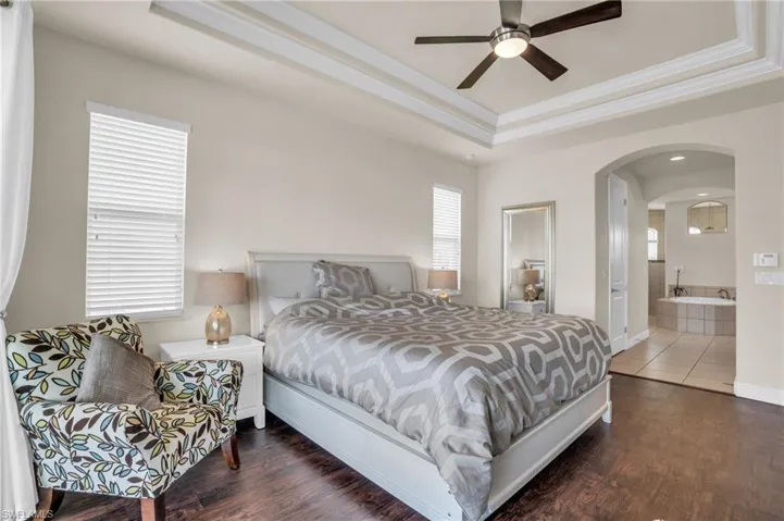Bedroom featuring ceiling fan, a tray ceiling, hardwood / wood-style floors, and ensuite bath