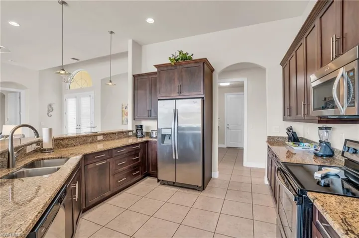 Kitchen featuring dark brown cabinets, decorative light fixtures, light tile floors, sink, and appliances with stainless steel finishes