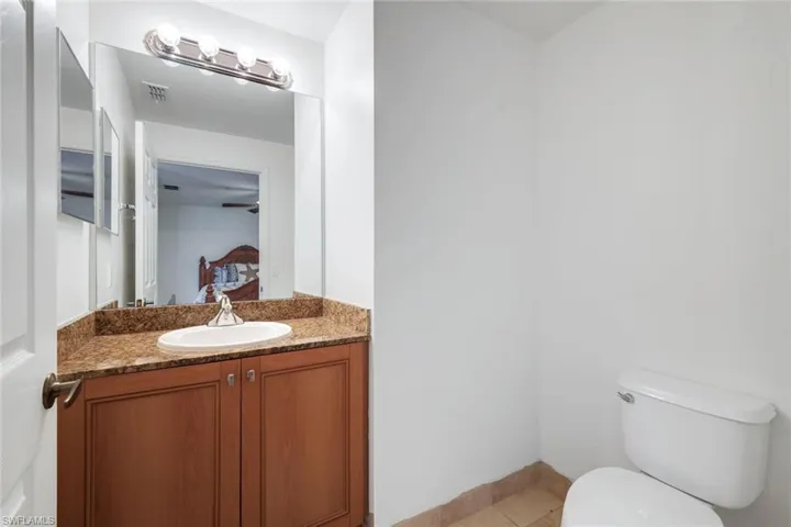 Bathroom featuring a wood-finish vanity with a built-in sink, stone countertop, large wall-mounted mirror, and a chrome light fixture