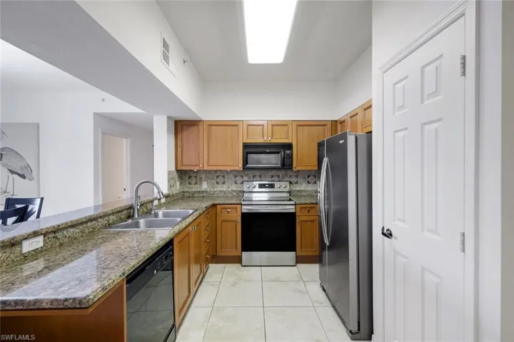 Well-appointed kitchen featuring granite countertops, wood cabinetry, stainless steel appliances, a tile backsplash, and tile flooring