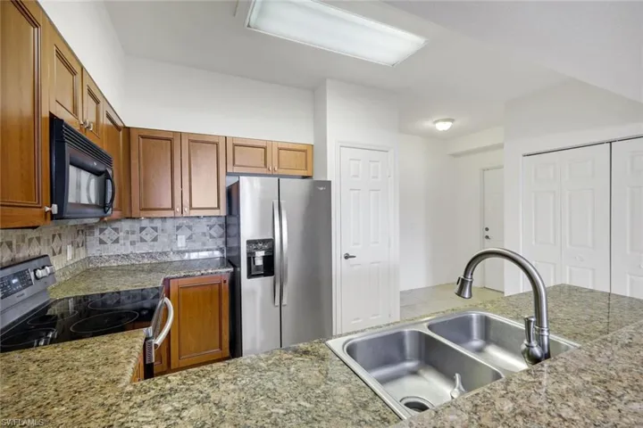 Kitchen featuring wood cabinetry, granite-finish countertops, stainless steel appliances, and a double basin sink with a gooseneck faucet