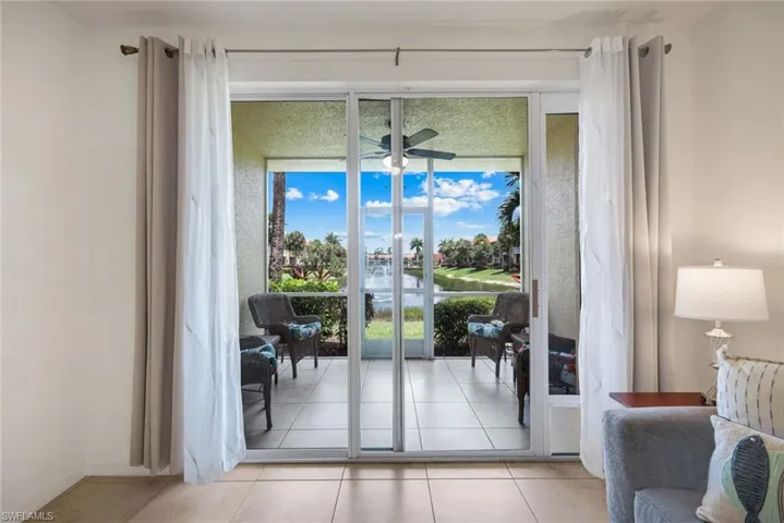 Expansive sliding glass doors open to a tiled balcony, featuring a ceiling fan and serene water views
