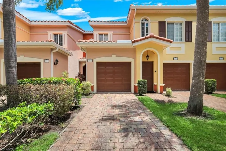 Mediterranean-style facade featuring terra cotta roof tiles, arched entryway, brown garage doors, paver driveway, and established landscaping