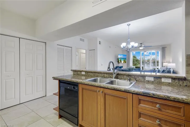 Kitchen featuring wood-finish cabinetry, granite countertops, a double basin stainless steel sink with a gooseneck faucet, and a black built-in dishwasher