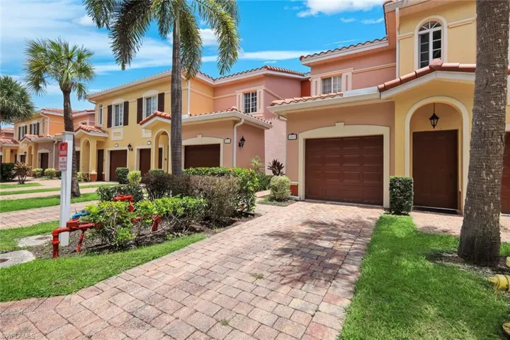 Mediterranean-inspired townhome featuring a paver driveway, attached garage, arched entryway, and terracotta-style roof tiles