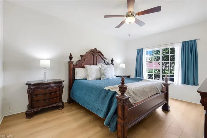Spacious bedroom featuring light wood-finish flooring, a ceiling fan with integrated lighting, and a large window with white muntins