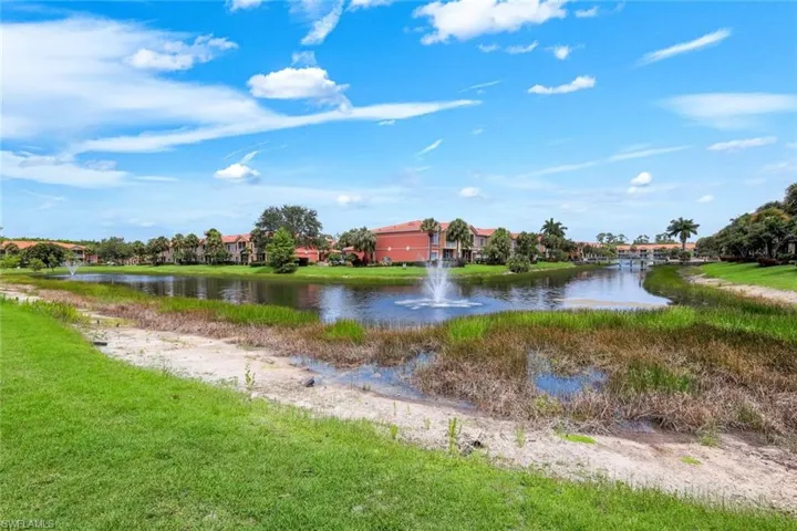 Community lake featuring a water fountain and surrounding residences with terracotta-style roofing