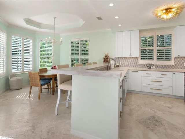 Kitchen featuring white cabinets, a breakfast bar area, healthy amount of natural light, decorative backsplash, and a tray ceiling