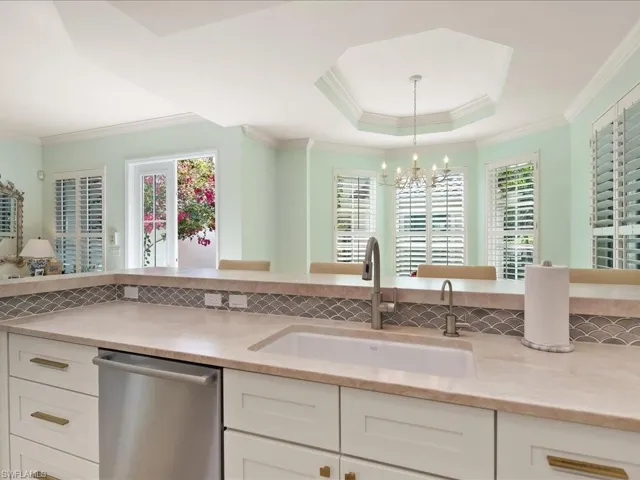 Kitchen featuring stainless steel dishwasher, a tray ceiling, white cabinets, light stone counters, and crown molding