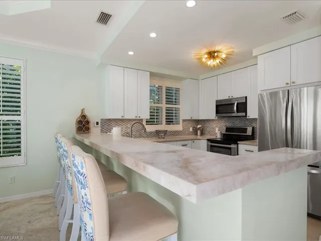 Kitchen featuring a kitchen bar, a peninsula, stainless steel appliances, white cabinetry, and light countertops