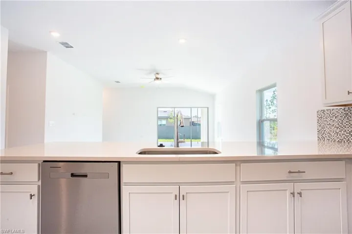 Kitchen with a sink, stainless steel dishwasher, white cabinetry, light countertops, and ceiling fan