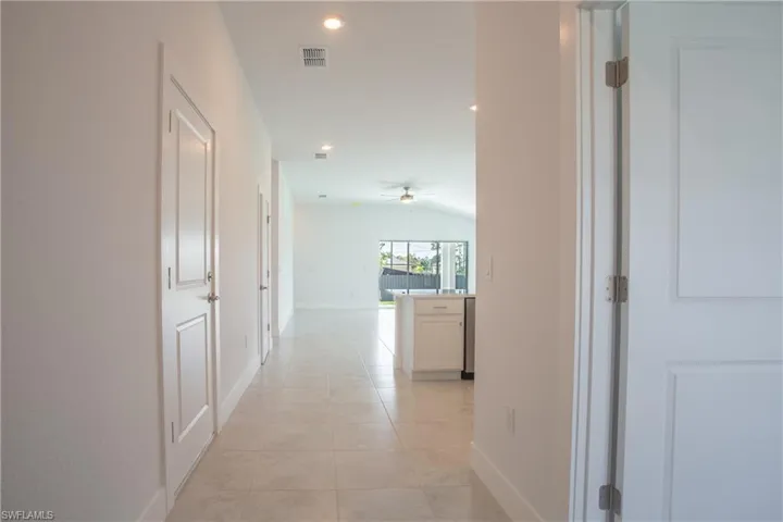 Hall featuring light tile patterned floors, visible vents, lofted ceiling, and baseboards