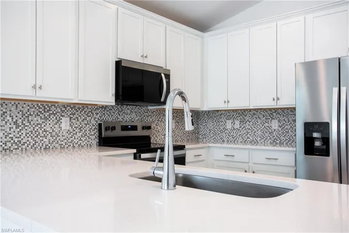 Kitchen featuring decorative backsplash, white cabinets, stainless steel appliances, and light countertops