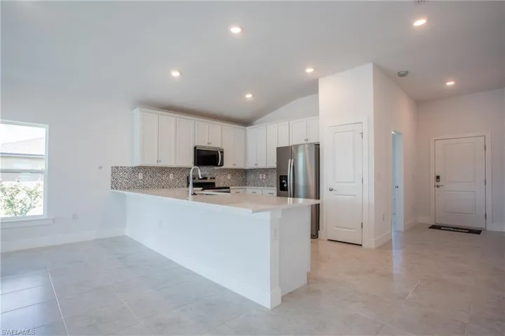 Kitchen with backsplash, light countertops, appliances with stainless steel finishes, a peninsula, and white cabinets