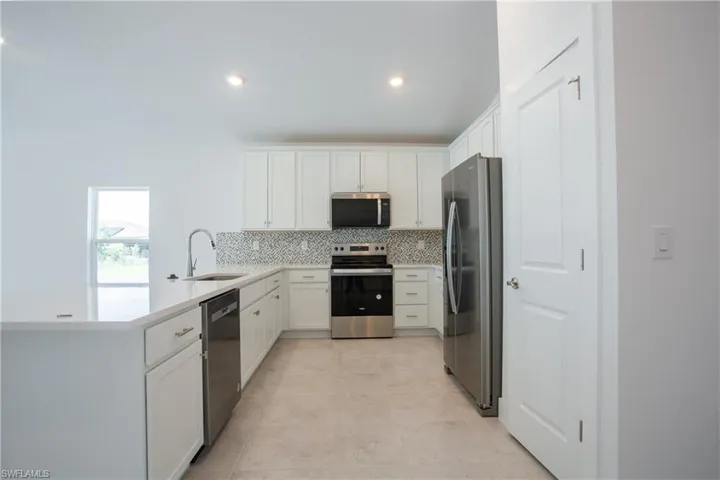 Kitchen with a sink, tasteful backsplash, appliances with stainless steel finishes, white cabinets, and light countertops