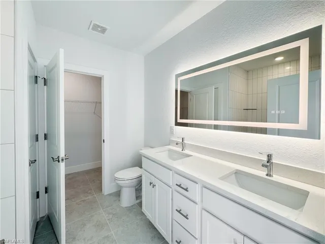 Bathroom with double vanity, a spacious closet, visible vents, and a sink