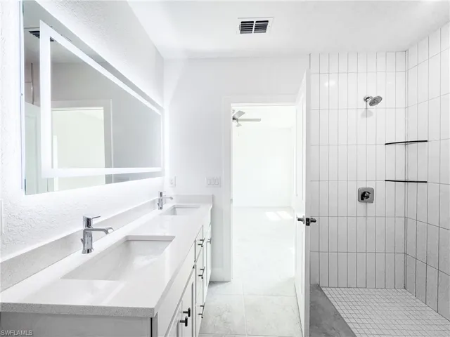 Full bathroom featuring double vanity, walk in shower, visible vents, and a sink