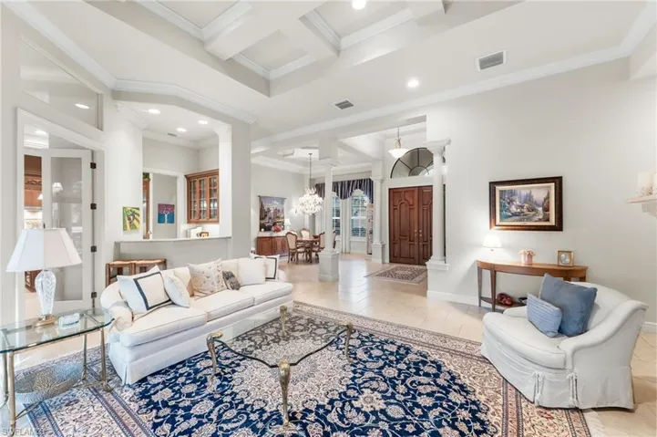 Tiled living room with coffered ceiling, ornamental molding, ornate columns, and recessed lighting