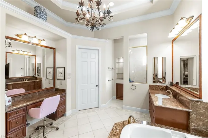 Full bath featuring ornamental molding, two vanities, hanging lights, light tile patterned floors, and a bathtub
