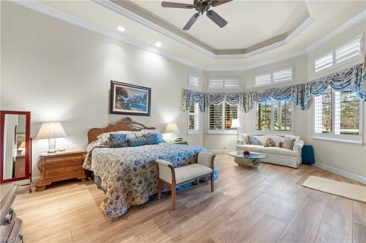 Bedroom featuring light wood-style flooring, ornamental molding, a ceiling fan, and a high tray ceiling