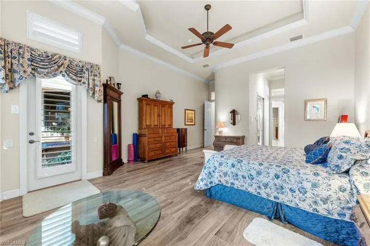 Bedroom with wood finished floors, a ceiling fan, a tray ceiling, and crown molding