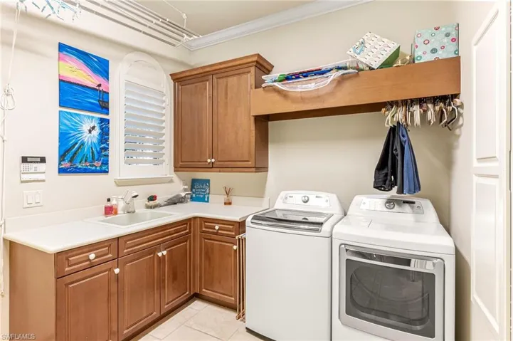 Laundry area featuring ornamental molding, cabinet space, washing machine and clothes dryer, and light tile patterned floors