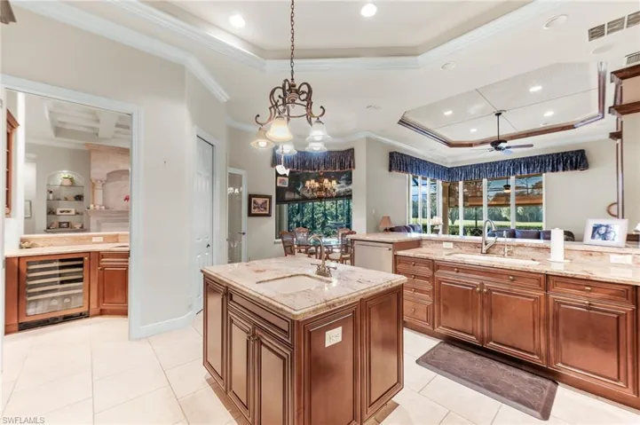 Kitchen featuring wood finish cabinets, a kitchen island with sink, ceiling fan, crown molding, and beverage cooler