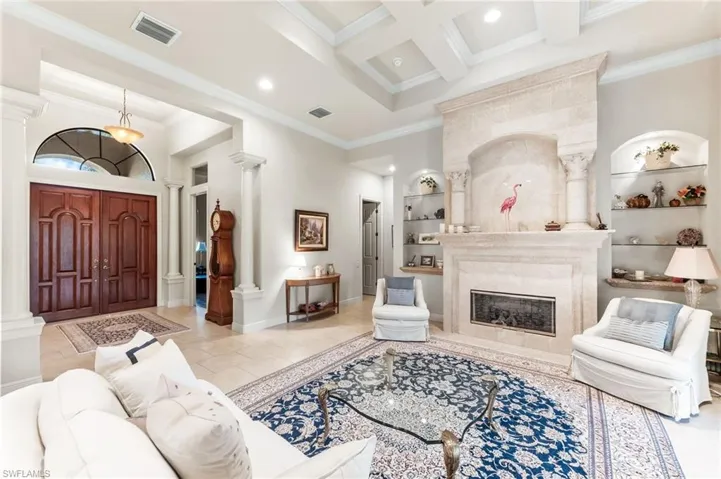 Living room featuring coffered ceiling, crown molding, recessed lighting, a fireplace, and decorative columns