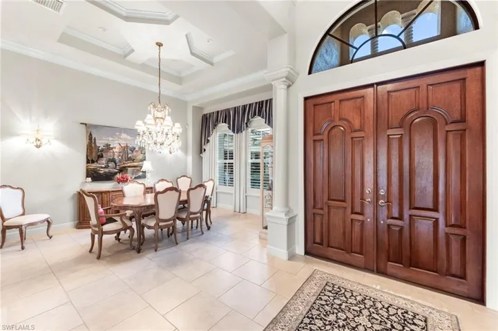 Entrance foyer featuring ornate columns, high coffered ceiling, ornamental molding, suspended lighting, and light tile patterned flooring