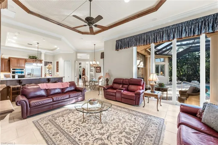 Living room featuring ceiling fan, a tray ceiling, ornamental molding, and suspended lighting