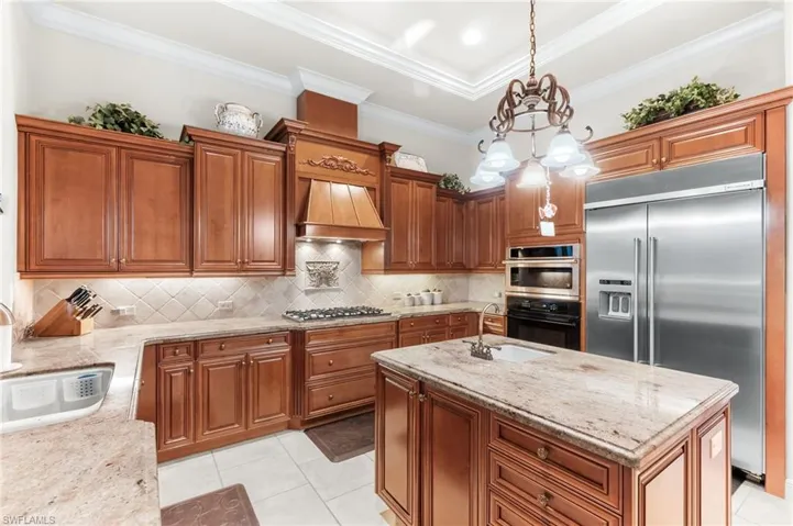 Kitchen featuring wood finish cabinets, stainless steel appliances, light stone counters, a kitchen island, and crown molding