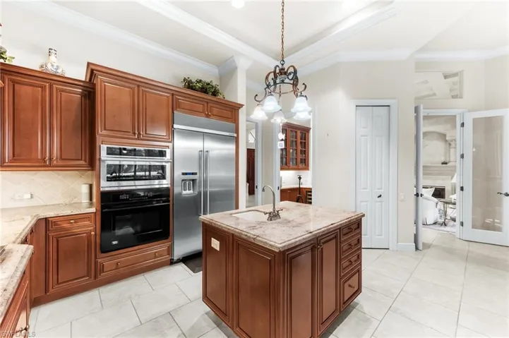 Kitchen with a kitchen island with sink, built in fridge, ornamental molding, a chandelier, and double wall oven