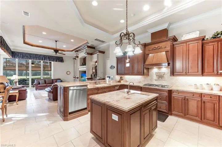 Kitchen with a tray ceiling, ornamental molding, wood finish cabinets, a peninsula, and pendant lighting