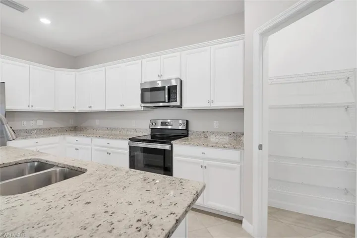 Kitchen featuring appliances with stainless steel finishes, white cabinets, light stone countertops, and recessed lighting
