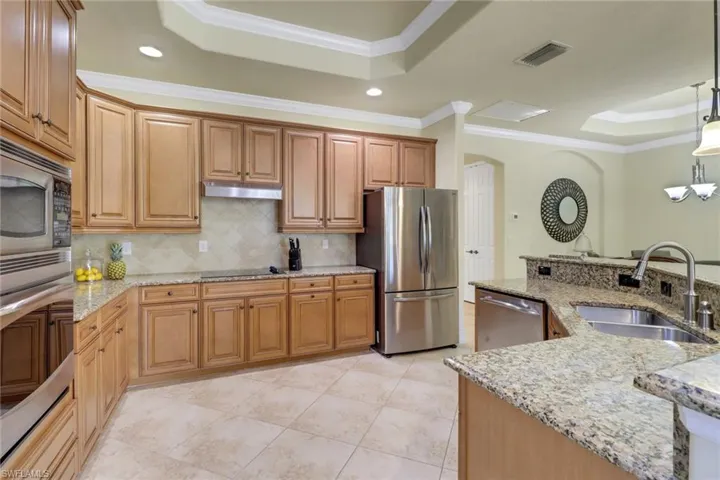 Kitchen featuring a tray ceiling, stainless steel appliances, ornamental molding, tasteful backsplash, and pendant lighting