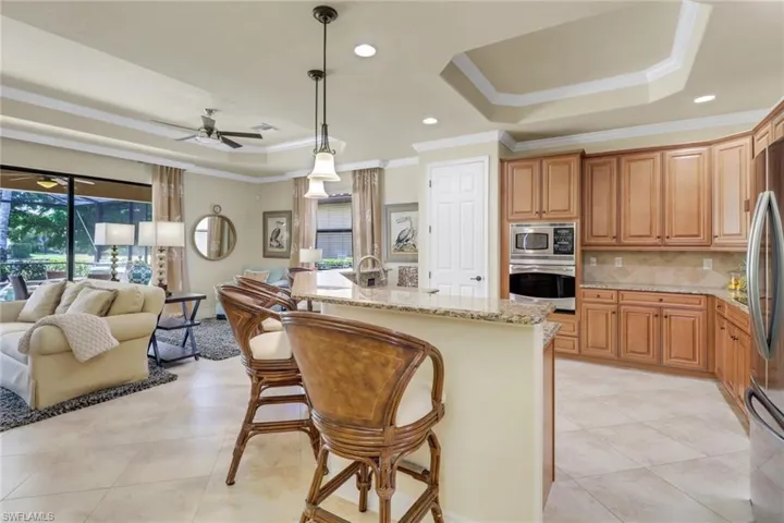 Kitchen with stainless steel appliances, a raised ceiling, crown molding, open floor plan, and light stone counters