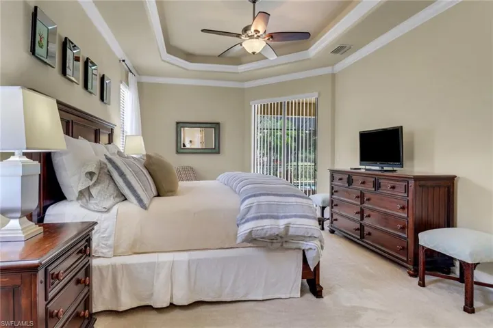 Bedroom with ornamental molding, a tray ceiling, light carpet, access to exterior, and ceiling fan