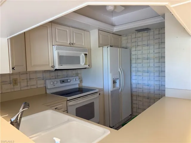 Kitchen with white appliances, light countertops, a tray ceiling, a ceiling fan, and ornamental molding