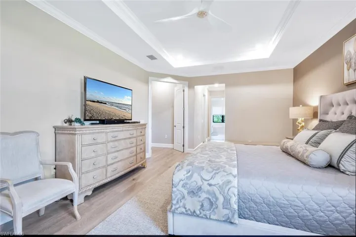 Bedroom with light hardwood / wood-style flooring, ornamental molding, ceiling fan, and a raised ceiling