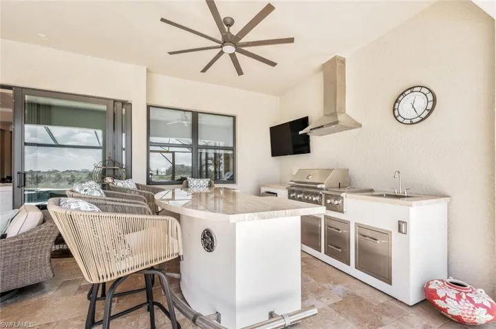 Kitchen featuring ceiling fan, light tile floors, wall chimney exhaust hood, a kitchen bar, and sink