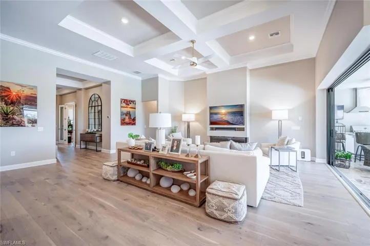 Living room with coffered ceiling, ceiling fan, ornamental molding, wood-type flooring, and beamed ceiling