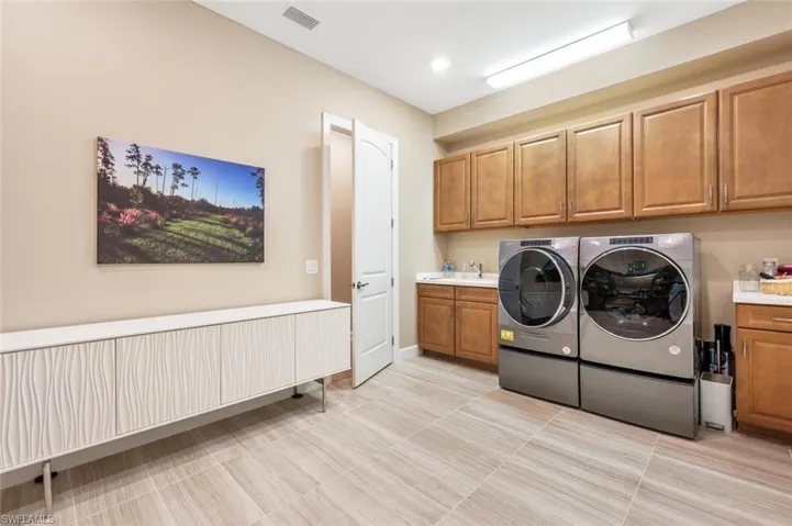Clothes washing area featuring washing machine and dryer, sink, cabinets, and light tile floors