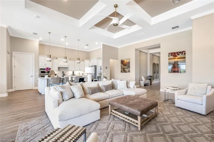 Living room with light hardwood / wood-style floors, ornamental molding, coffered ceiling, and ceiling fan